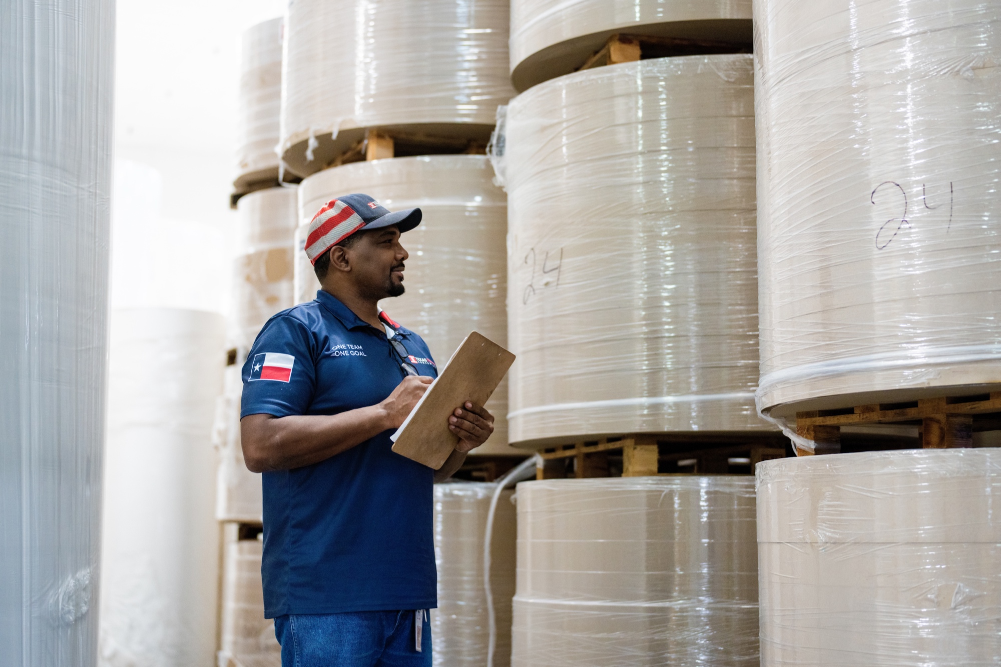 Warehouse worker inspecting paper roll inventory with a clipboard